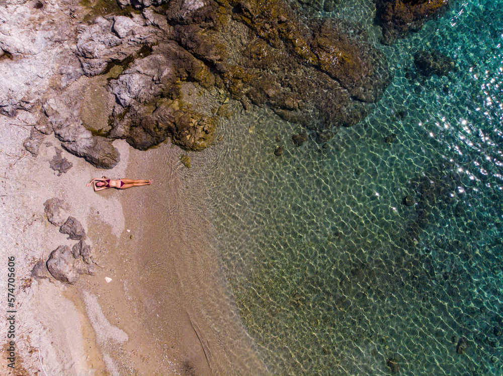 top down view of a girl in a bikini lying on the sand on the seashore; relaxing on a paradise beach as seen from a drone; a beautiful model lying on the sand