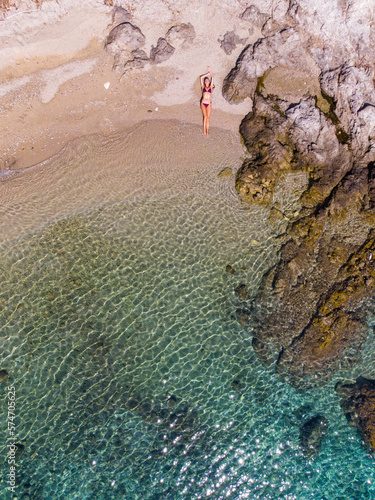 top down view of a girl in a bikini lying on the sand on the seashore; relaxing on a paradise beach as seen from a drone; a beautiful model lying on the sand