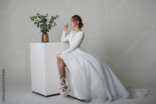 A beautiful young bride model in long lace dress in minimalist white studio interior. Wedding photography.