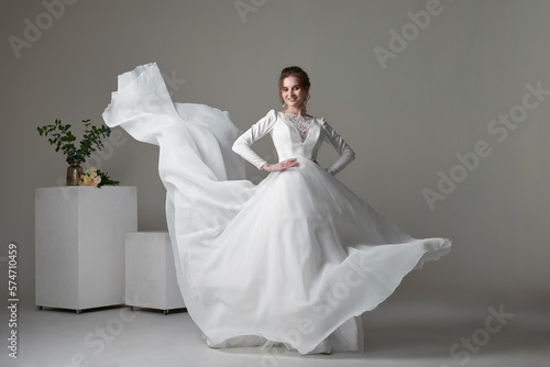 A beautiful young bride model in long lace dress in minimalist white studio interior. Wedding photography.