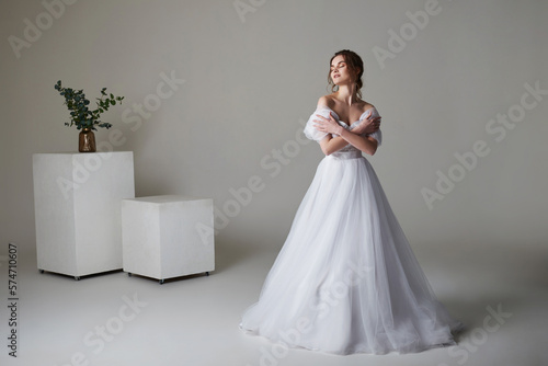 A beautiful young bride model in long lace dress in minimalist white studio interior. Wedding photography.