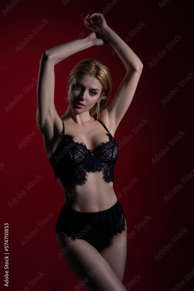 Sensual young woman posing with sexy slim body. Lingerie model in sexy bra and panties. Lace black lingerie. Breast in sexy bra, natural boobs. Sensual model in sexy lingerie isolated on red studio.
