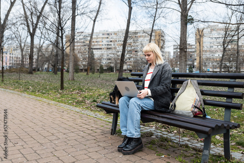 Young university girl sitting on bench with adopted dog working on laptop. She left the apartment for her student roommate boyfriend they need privacy because they share rented apartment or room