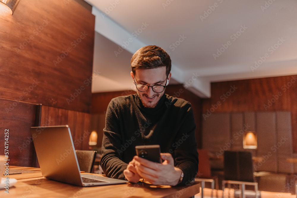 Happy young businessman working on a laptop and smartphone in a cafe Happy young businessman working on a laptop and smartphone in a cafe