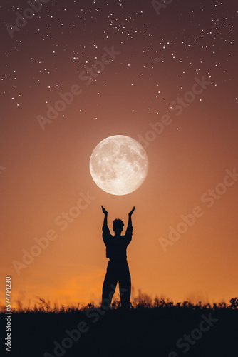 Fantastic photo of the silhouette of a girl holding the moon in her hands. Girl at sunset. Abstraction with starry sky. A person who dreams