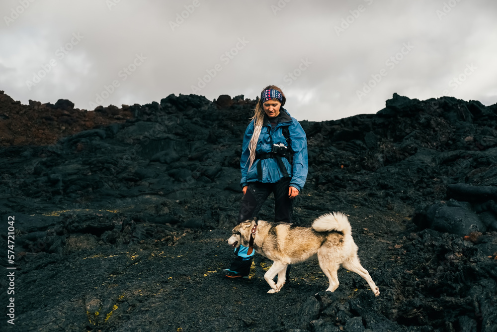 Traveler female walking with her dog on the frozen lava of volcano. Hiking in the mountains of Kamchatka