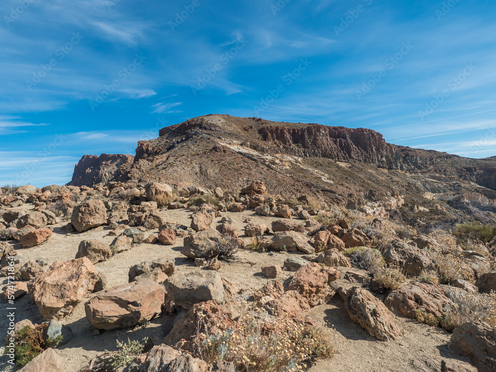Peak Alto de Guajara volcano with lava rock boulders and dry vegetation, view at hiking trail to the summit. Colorful dry volcanic scenic landscape at national park of Teide, Tenerife, Canary Islands.