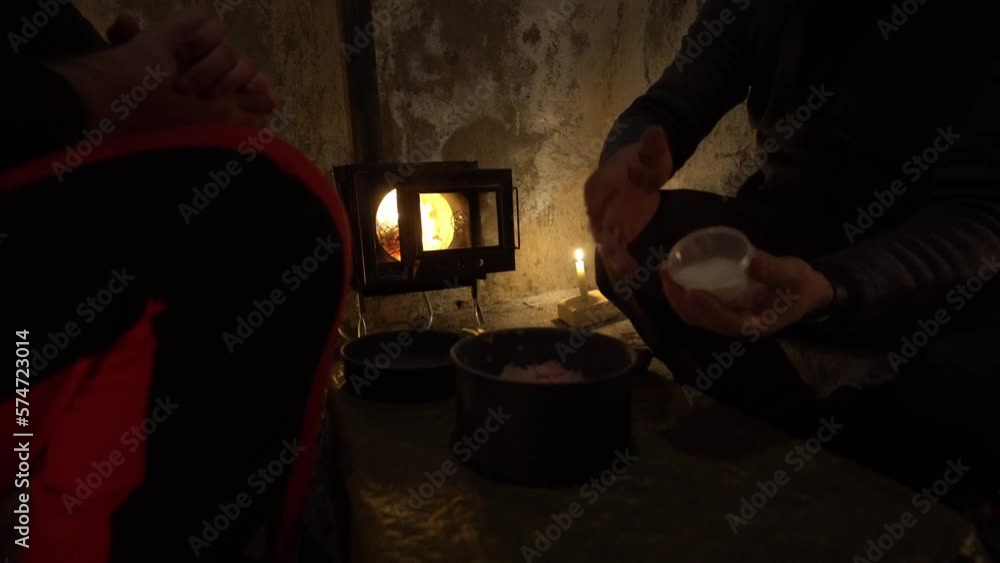 They cook food in unusual camping conditions. An old hut, a fire is burning in a camp stove and candles are nearby. Old walls. The guy decided to put minced meat with onions in a camp pot and stir. They cook food in unusual camping conditions. An old hut, a fire is burning in a camp stove and candles are nearby. Old walls. The guy decided to put minced meat with onions in a camp pot and stir.