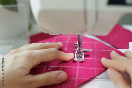 close up, woman sews clothes or accessories from pink fabric in workshop. creative sewing studio, handmade designer fashion house atelier. women's small business and home office work