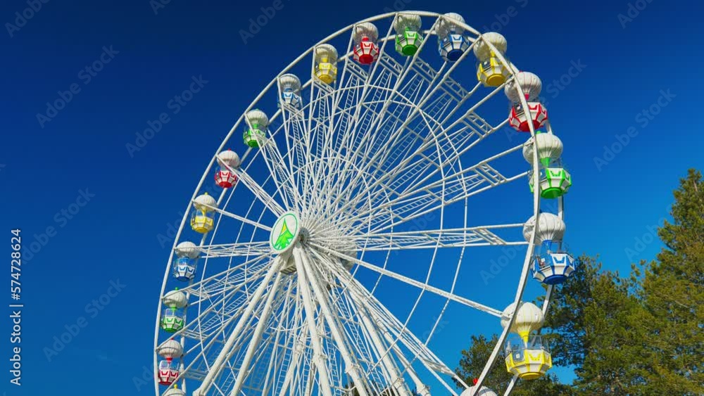 The Ferris wheel on the blue clear sky is slowly spinning The Ferris wheel on the blue clear sky is slowly spinning
