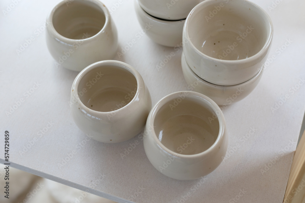 creamy white background with ceramic pots and cups, shallow depth of field with focus on the first cups creamy white background with ceramic pots and cups, shallow depth of field with focus on the first cups