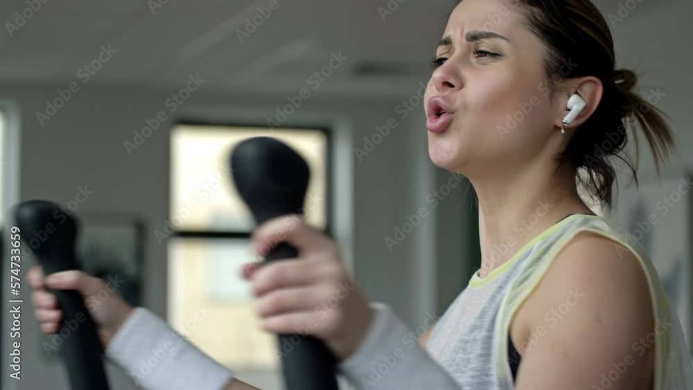 Young beautiful woman with headphones is engaged in a simulator in the gym. Sports and music. Concept of sport and healthy lifestyle. Young beautiful woman with headphones is engaged in a simulator in the gym. Sports and music. Concept of sport and healthy lifestyle.
