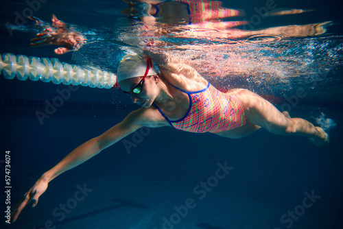 Activity. Young sportive woman  professional swimmer training in swimming pool indoor. Wearing cap and goggles. Underwater view. Concept of sport  endurance  competition  energy  healthy lifestyle