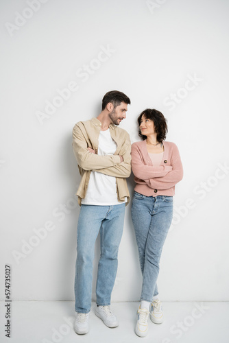 Brunette couple crossing arms while standing on white background.