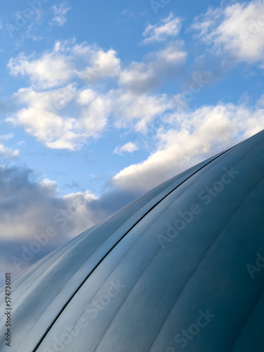 Tennis dome creates a beautiful curved shape against a blue sky with clouds during golden hour.