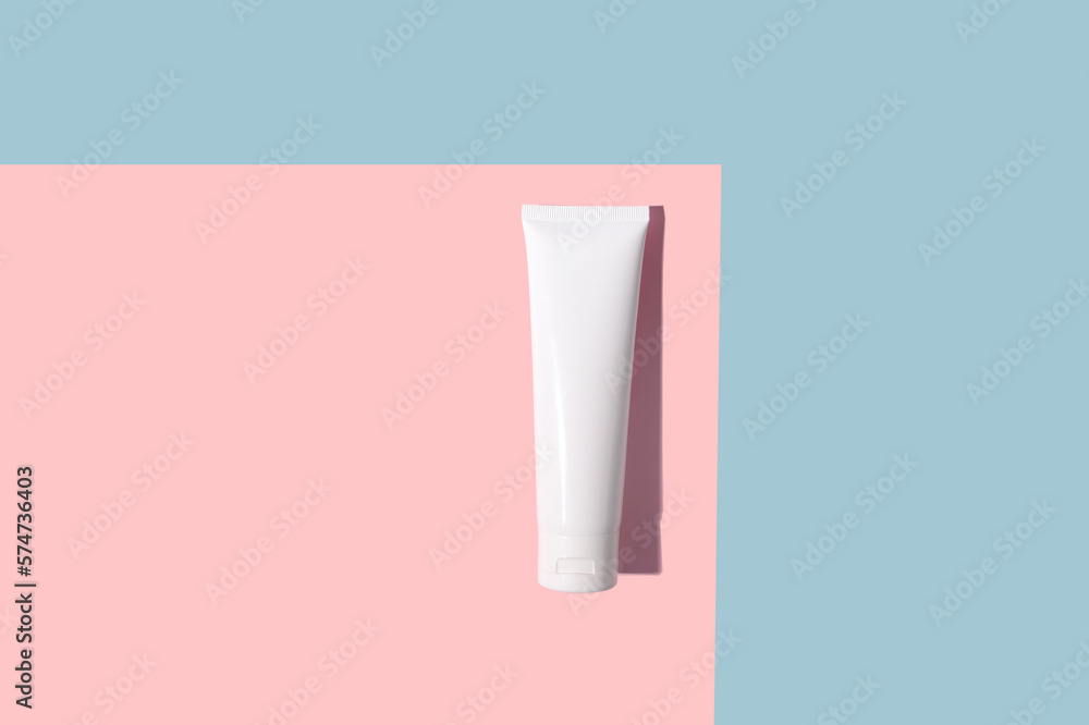 White cosmetic tube of cream with a hard shadow on a pink and blue background. White cosmetic tube of cream with a hard shadow on a pink and blue background.