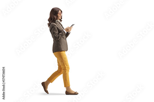 Full length profile shot of a young woman in formal clothing walking and using a smartphone