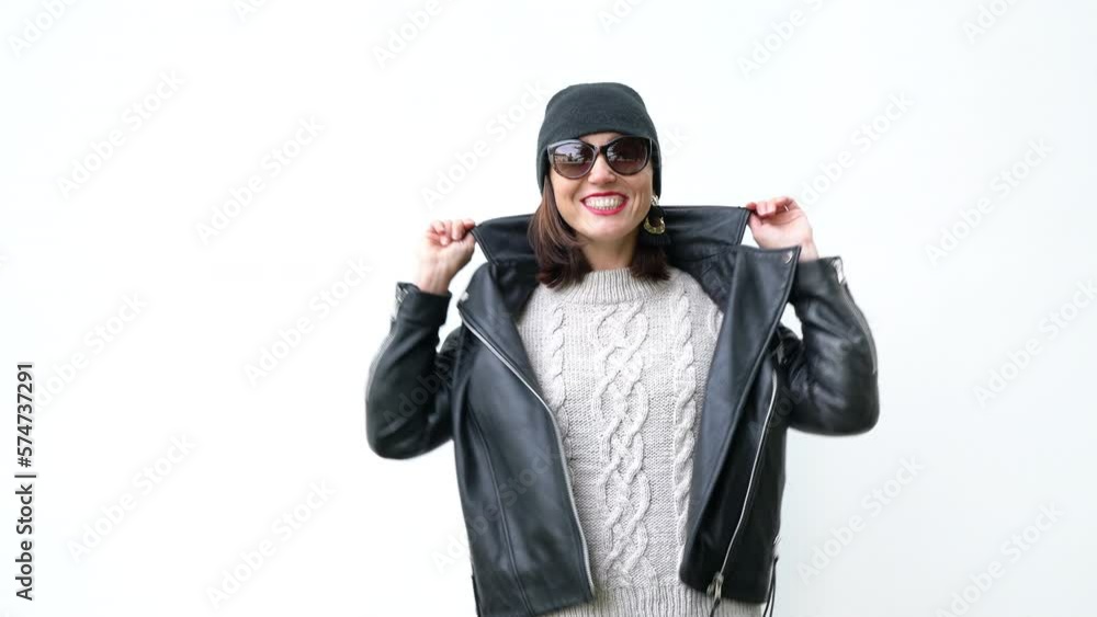 Beautiful female cheerfully smiling and posing in front of white wall dressed in knitted sweater, black leather jacket and Beanie hat 4K footage Beautiful female cheerfully smiling and posing in front of white wall dressed in knitted sweater, black leather jacket and Beanie hat 4K footage