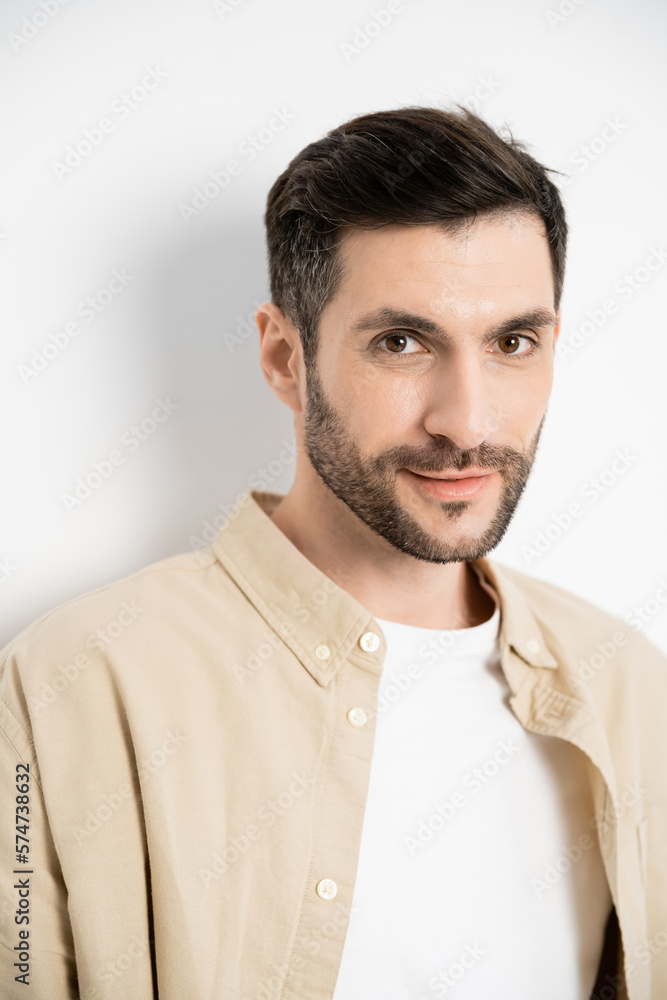 Obraz premium Portrait of brunette man in beige shirt looking at camera on white background.