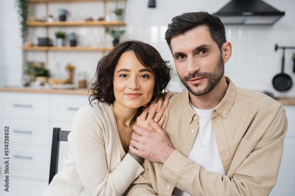 Smiling man looking at camera and touching hand of wife in kitchen. Smiling man looking at camera and touching hand of wife in kitchen.