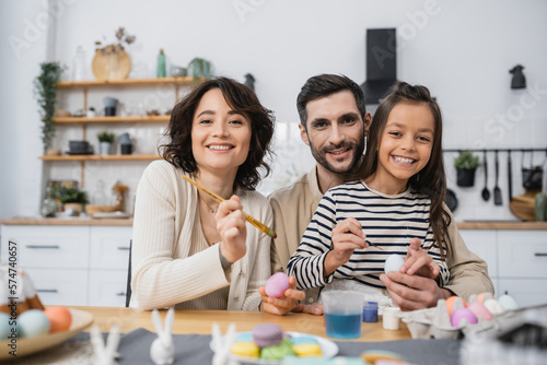 Smiling family looking at camera while coloring Easer eggs in kitchen.