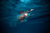 Front crawl. Speed. Young woman, professional swimmer in goggles and cap training, swimming in pool indoors. Underwater view. Concept of sport, endurance, competition, energy, healthy lifestyle
