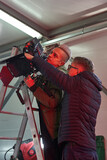 two caucasian men hold and set up a professional camera under the ceiling of the film set on a ladder