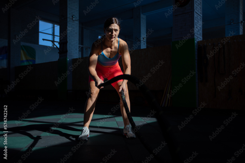 Athletic woman doing double wave exercise with ropes in crossfit gym. Athletic woman doing double wave exercise with ropes in crossfit gym.