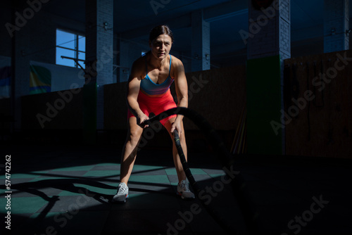 Athletic woman doing double wave exercise with ropes in crossfit gym.
