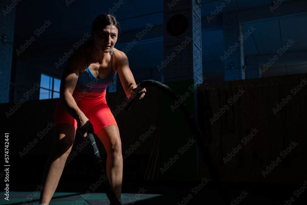 Athletic woman doing double wave exercise with ropes in crossfit gym. Athletic woman doing double wave exercise with ropes in crossfit gym.