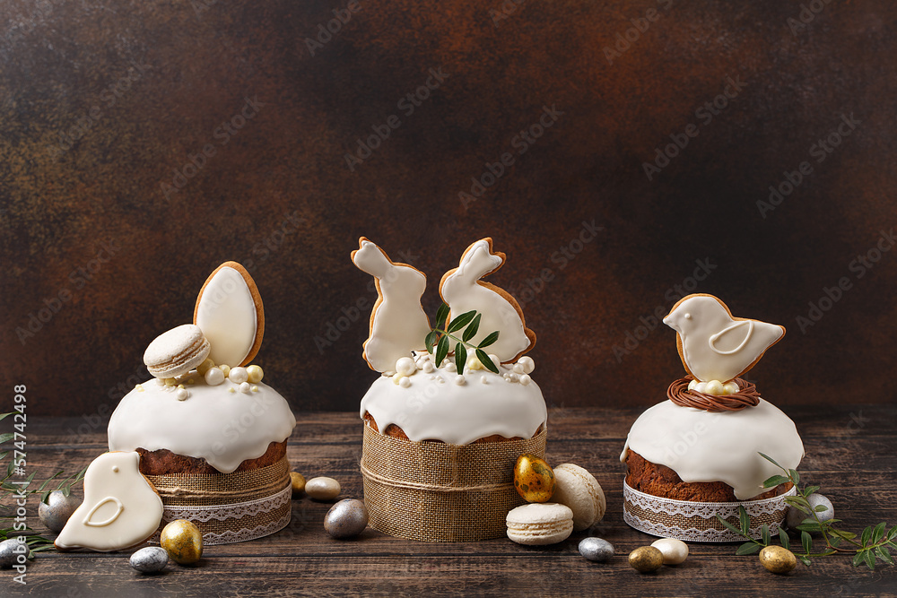 Φωτογραφία Set of traditional easter cakes with icing, decorated with gingerbread cookies in shape of rabbits and birds over dark brown background