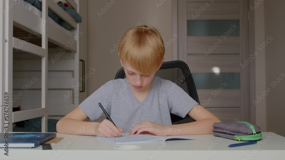 Handsome boy is studying - doing homework. Cute boy at home sitting at the table. Home school for children. Learn for yourself. Smart schoolboy performs his task in the room. Handsome boy is studying - doing homework. Cute boy at home sitting at the table. Home school for children. Learn for yourself. Smart schoolboy performs his task in the room.