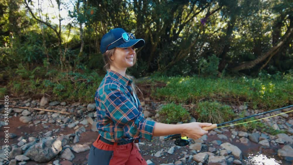 Fisherwoman casts the line. Pretty woman angler wearing casual fishing clothes standing near the river and casting the line Fisherwoman casts the line. Pretty woman angler wearing casual fishing clothes standing near the river and casting the line