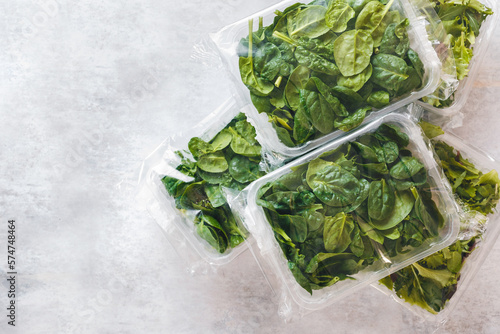 Spinach and Japanese mizuna packaged in clear plastic containers on rustic background. Top view, blank space
