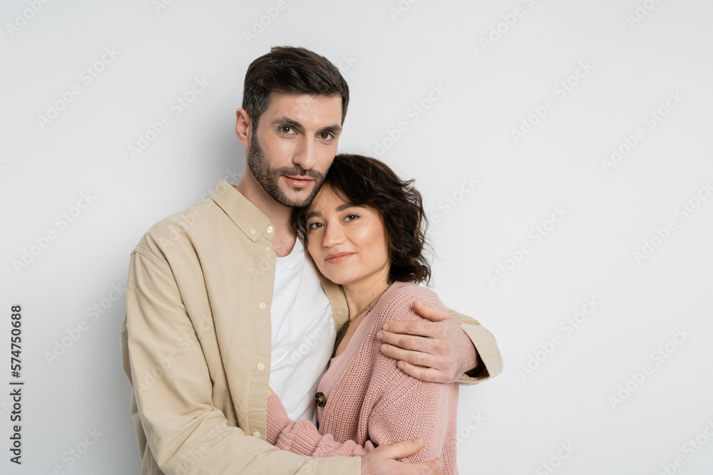 Bearded man hugging wife and looking at camera on white background. Bearded man hugging wife and looking at camera on white background.
