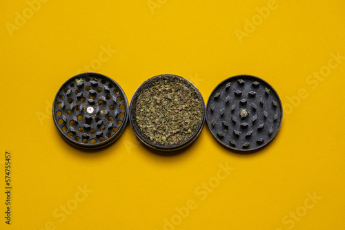 Close up of high quality marijuana bud chopped inside a grinder on a yellow background. Cool minimal flat lay, copy space.