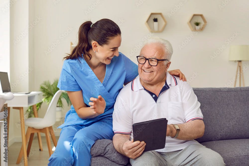 custom made wallpaper toronto digitalYoung friendly female caregiver and senior man using digital tablet together in nursing home. Woman in medical uniform and elderly man are sitting on sofa and discussing modern technology.