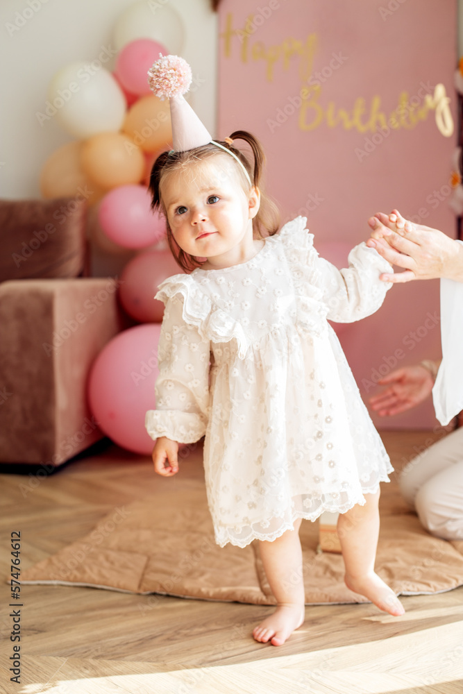 Fototapeta premium Mother holding hand of toddler girl and celebrating birthday. Baby learning to walk