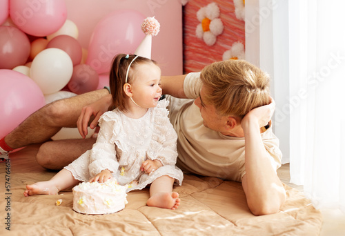 One year old little girl with daddy solemnize birthday and eat cake. Happy laughter. Family and love photo