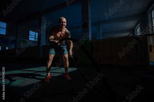 Athletic man doing double wave exercise with ropes in crossfit gym.