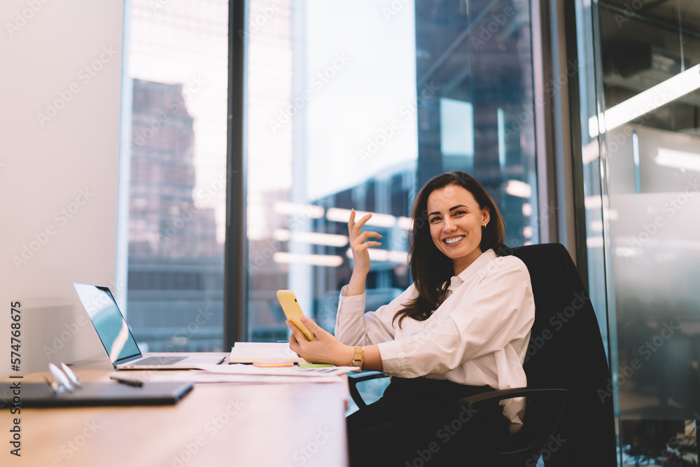 Smiling woman sitting at table with laptop and smartphone in office Smiling woman sitting at table with laptop and smartphone in office