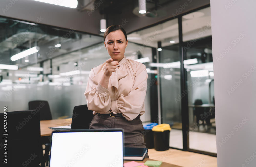 Serious man standing near laptop in office with raised hand Serious man standing near laptop in office with raised hand