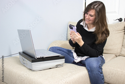 A woman with laptop and phone working from home on the couch