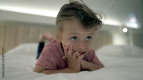Hypnotized little boy watching TV screen at night laying in bed. Close up face of small male kid staring at cartoons