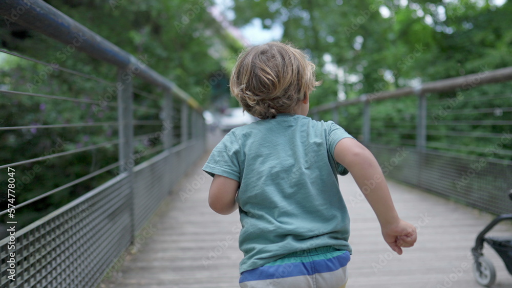 One active small boy running outdoors at park crossing bridge. Back of child runner in slow motion outside exercising. Sportive kid One active small boy running outdoors at park crossing bridge. Back of child runner in slow motion outside exercising. Sportive kid
