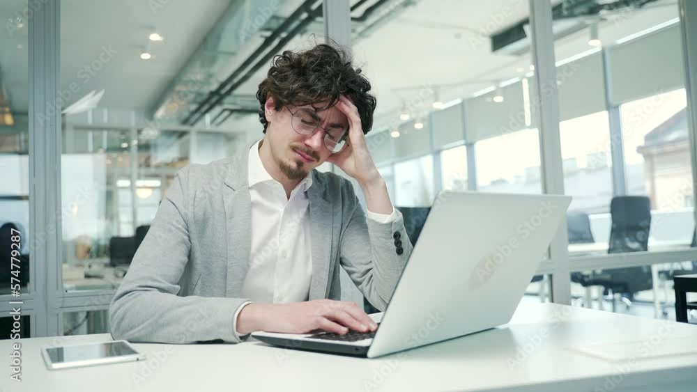Portrait of sad business man freelancer suffering headache painful feelings chronic migraine pressure working on computer at modern glass office Stressed entrepreneur feels hurt at workplace indoors Portrait of sad business man freelancer suffering headache painful feelings chronic migraine pressure working on computer at modern glass office Stressed entrepreneur feels hurt at workplace indoors