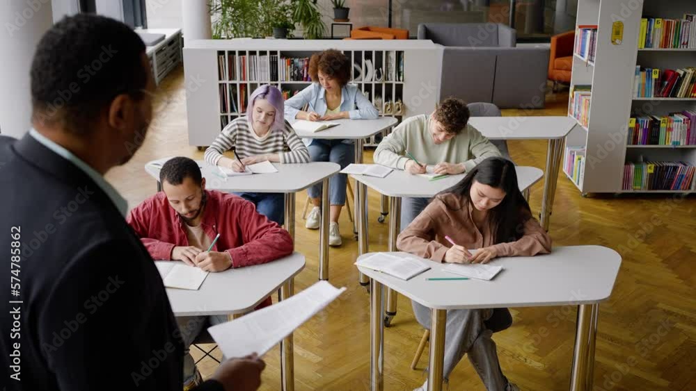 Diverse young students writing lecture under the dictation of a young African American professor Diverse young students writing lecture under the dictation of a young African American professor