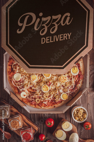 Brazilian pizza with mozzarella, ham, onion, olive, boiled eggs and oregano  in a delivery box(Pizza portuguesa) - Top view.