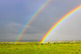 Bright colors of double rainbow rising from a meadow with dark rain clouds in the background