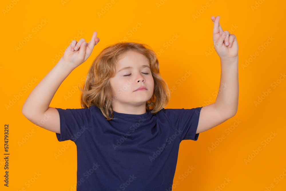 Kid crossed fingerson yellow isolated studio background. Child closed eyes, with good luck gesture. Lucky boy, hope and wish.